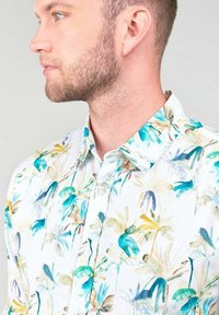 Korte mouw shirt met een witte achtergrond, voorzien van een kleurrijk aquarel bloemenpatroon in tinten blauw, groen en geel.