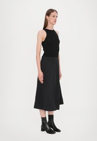 Musta ribbi tank top, jossa on olkaimien leikkaukset, yhdistettynä lanteilta valuvaan mustaan midi-hameeseen ja nilkkapituisiin mustiin nahkakengillä varustettuihin korkokenkiin.
