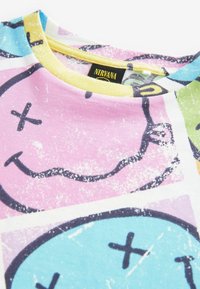 T-shirt en coton à manches courtes arborant des visages souriants colorés sur un fond pastel rose et bleu, avec un col jaune. Étiquette de la marque visible.