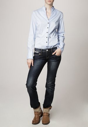 Lichtblauw overhemd met lange mouwen, textuur met polka dots en een gerimpelde kraag, gecombineerd met een donkere jeans en bruine enkellaarzen met grijze boorden.