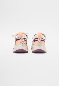 Calzature con un design beige chiaro e pesca, tessuto a rete, accenti viola e un sistema di lacci sicuro con una linguetta sul tallone.