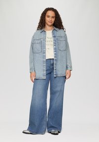 Lichtblauwe denim overhemd met voorklauwen, gecombineerd met een crèmekleurig t-shirt en wijde blauwe jeans. Schoenen met zilveren accenten maken de outfit compleet.