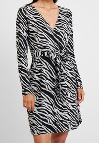 Czarna i szara sukienka w paski zebry, z dekoltem w serek, długimi rękawami i materiałowym paskiem w talii. Miękka tekstura i dopasowany krój.