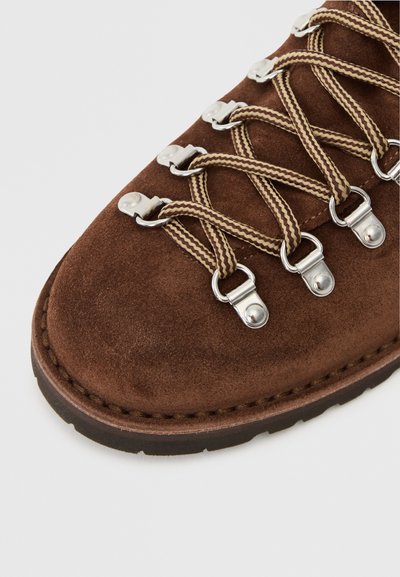 Brown suede hiking boot featuring silver metal eyelets, overlaid with dark brown laces and a stitched rubber sole.