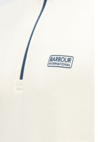 Fehér pulóver negyed cipzárral, a cipzár mentén kék díszítéssel és egy kék "Barbour International" logóval a mellrészen.