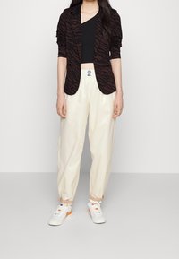 Svart och brun zebra-randig blazer, svart topp, krämfärgade tapered byxor och vita sneakers med orange detaljer. Avslappnad, modern outfit.