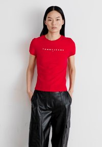 Červené bavlněné tričko s krátkými rukávy a bílým logem "TOMMY JEANS", zkombinované s černými koženými cargo kalhotami. Minimalistický design.
