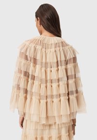 Transparent ljusbeige topp med lager av volanger i tyl, med rund halsringning och texturerad detaljering genom hela designen.