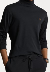 Svart turtleneck sweatshirt med långa ärmar, som har en liten broderad logotyp. Tillverkad av mjukt material med en avslappnad passform och ribbade manschetter.