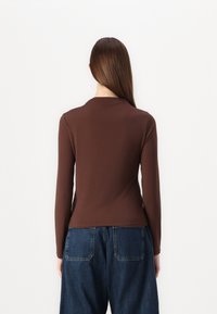 Brun långärmad topp med en figurnära design, gjord av ett slätt tyg, i kombination med lösa blå jeans. Minimalistisk stil utan synliga utsmyckningar.