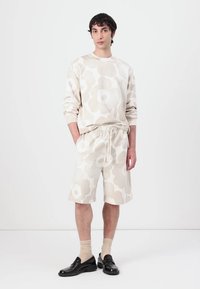 Hellblaues Sweatshirt und Shorts-Set mit großen Blumenmustern, aus weichem Material gefertigt. Schwarze Schuhe runden das Outfit ab.