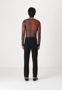 Top vermelho de malha transparente, com mangas longas e design ajustado, usado com jeans pretos de pernas direitas e sapatos pretos, visto de costas.