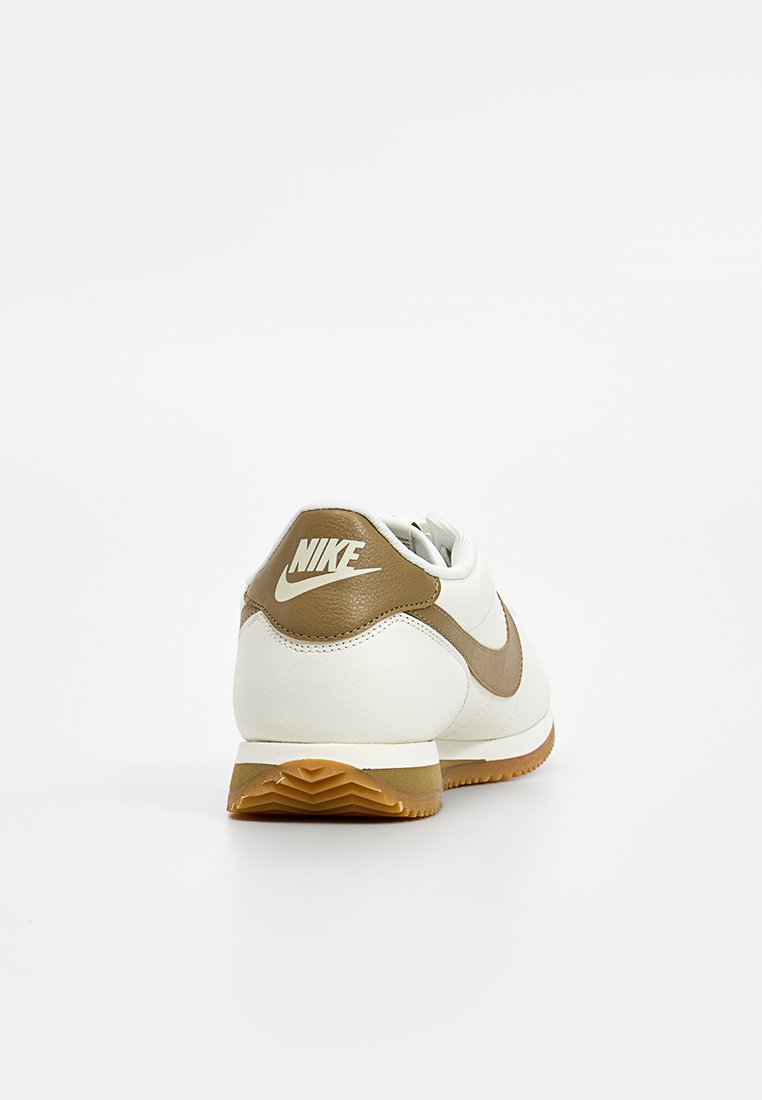 Nike-Sneaker mit einem Obermaterial aus weißem Leder und braunen Akzenten, einer runden Form und einer strukturierten Gummisohle. Auf der Rückseite befindet sich ein Logodetail.