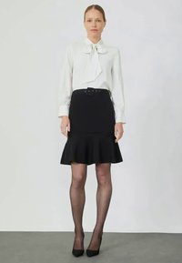Biała bluzka z kokardą i czarna rozkloszowana spódnica z paskiem i gładkim materiałem. Czarne szpilki i rajstopy w neutralnym odcieniu.
