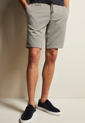 Light gray shorts with a relaxed fit, drawstring waistband, and side pockets, paired with navy suede sneakers.