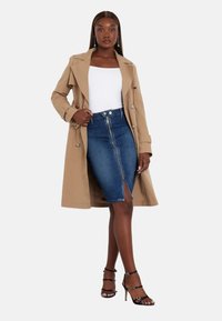 Bežinis paltas su dvigubais sagčių užsegimais, vilkimas virš baltos palaidinės ir mėlyno džinsinio sijono su priekiu užtrauktuku ir šoniniu plyšiu. Juodi juostiniai aukštakulniai.