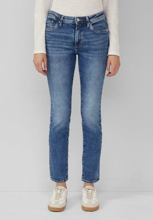 Dark blue jeans in a slim fit. Features include five pockets, subtle fading, and a button closure. Styled with light-colored sneakers.