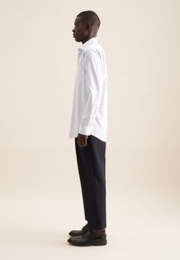 Camicia button-up a strisce blu chiaro con taschino sul petto, abbinata a pantaloni blu navy e scarpe stringate nere, esposta su uno sfondo neutro.