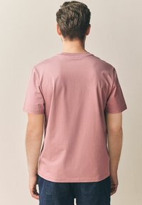 Kortærmet t-shirt i blød lyserød bomuld, med rund hals, afslappet pasform og diskrete stikninger, set fra ryggen.