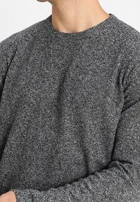 Suéter gris texturizado con cuello redondo y mangas largas. Presenta una tela de punto con un patrón sutil y una apariencia suave.