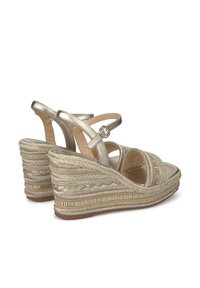 Sandales compensées en or métallique avec des brides croisées, une texture tissée et une semelle décorative en corde tressée. Bride de cheville réglable incluse.