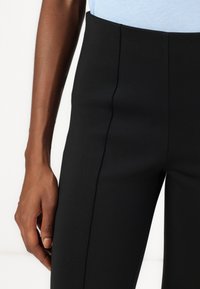 Pantalons ajustés noirs avec une texture lisse et une silhouette allongée, dotés de coutures avant et d'une taille haute.