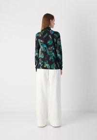 Bluză florală cu mâneci lungi, cu modele verzi și portocalii pe un fundal negru, asortată cu pantaloni largi albi, având un tiv curat.