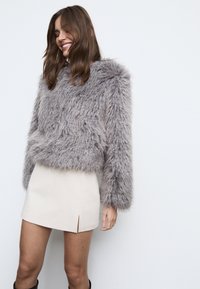 Kunstpels, kort grå jakke med lange ærmer, blød tekstur, kombineret med en kort beige nederdel med slidse foran.