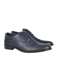 Par de zapatos formales de cuero azul oscuro para hombre con cordones y tacones bajos negros, mostrados en un ligero ángulo sobre un fondo blanco.