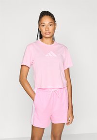 Rosa gekürztes T-Shirt mit dezentem Logo und passenden pinkfarbenen Shorts mit Seitenstreifen. Weicher Stoff und lockere Passform für Komfort.