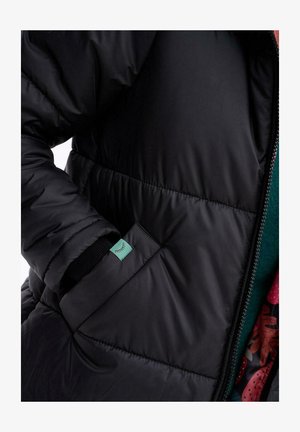 Czarna puchówka z pikowanym wzorem, z zapięciem na zamek oraz boczną kieszenią z małą zieloną metką. Widoczna podszewka z kwiatowym wzorem.