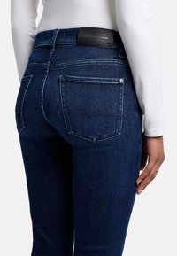 Jeans in denim indaco scuro con vita alta, dotati di tasche posteriori e un'etichetta in pelle nera sul cinturino. Design minimalista.