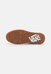 Suela de zapatilla Vans en goma marrón con un patrón de agarre texturizado. Presenta un logo blanco con ángulos afilados y contornos contrastantes.