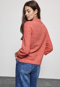 Pullover a maglia con trama rossa e bianca, dotato di colletto e maniche lunghe, abbinato a jeans in denim blu. La maglia ha una vestibilità comoda e spacchi laterali.