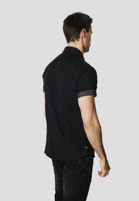 Camiseta negra de manga corta con puño texturizado negro, presenta una tela suave y un branding sutil en el hombro y el dobladillo.