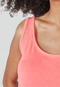 Débardeur corail avec larges bretelles, encolure dégagée et texture douce ; coupe ajustée mettant en valeur les épaules et le décolleté.