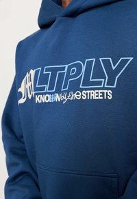 Felpa blu realizzata in misto cotone, caratterizzata da grandi testi bianchi e azzurri che recitano "ALTPLY KNOWN by the STREETS." Include una tasca frontale.