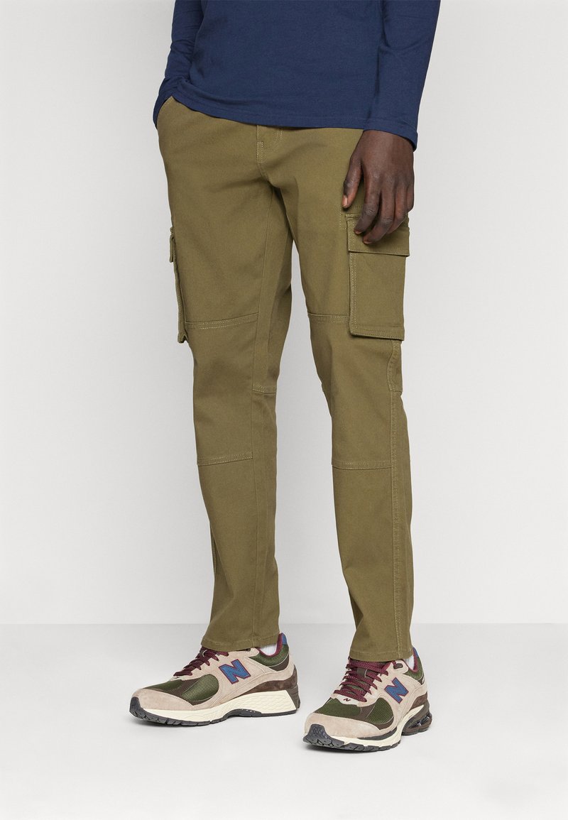 Pantalones cargo en algodón verde olivo, con bolsillos laterales y detalles cosidos, combinados con zapatillas multicolor y una camisa de manga larga azul marino.