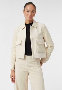 Beige cropped jack gemaakt van een gestructureerd materiaal, met een puntige kraag, twee voorzakken en een rits aan de voorkant.