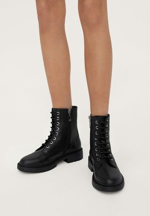 Black leather ankle boots with a round toe, lace-up front, and side zipper. Features metal eyelets and a textured rubber sole.
