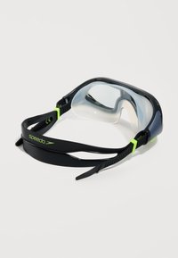 Μαύρα και πράσινα γυαλιά κολύμβησης Speedo με διάφανα φακούς και ρυθμιζόμενο λουράκι, τοποθετημένα σε λευκό φόντο.