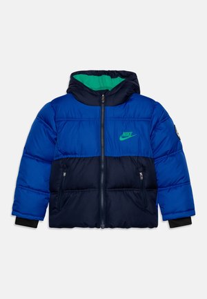 Veste matelassée Nike pour enfants, bleu et marine, avec logo vert, fermeture éclair devant, deux poches zippées et capuche doublée en tissu vert.