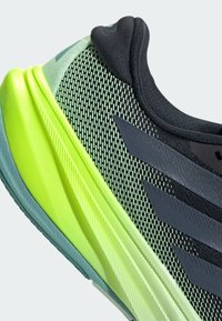 Černá a zelená sportovní bota s prodyšným síťovaným svrškem, vrstvenou podrážkou s texturovanými akcenty a výraznými černými pruhy po straně.