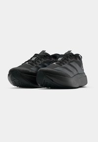 Ténis desportivos pretos com parte superior texturizada, biqueira reforçada, sola grossa e atacadores contrastantes. Logótipo exibido no lado e no calcanhar.