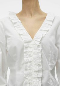 Witte katoenen blouse met een diepe V-halslijn en een ruches-trim in het midden, evenals ruches langs de halslijn. Soepele textuur.