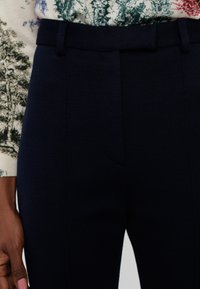 Námornícky modré nohavice s prispôsobeným strihom a hladkou textúrou, s plochým predným dielom, pútkami na opasok a bočnými vreckami. Textúrovaná tkanina sa kombinuje so vzorovaným vrchom.