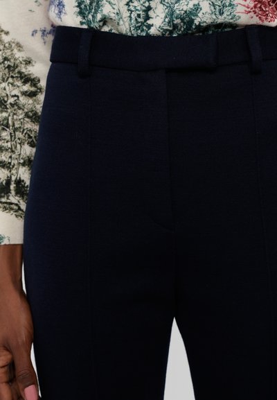 Navy blue tailored pants with a smooth texture, featuring a flat front, belt loops, and side pockets. Textured fabric blends with patterned top.