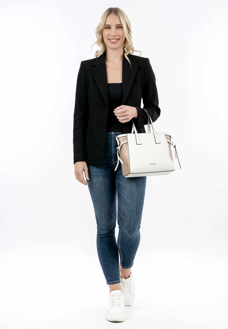 Sac à main blanc avec une accent texturé beige, forme structurée, poignées supérieures et quincaillerie en argent. Le modèle porte un blazer noir, un débardeur et un jean.