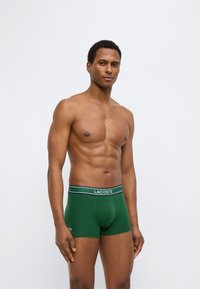 Πράσινα σλιπ μποξέρ με μαύρη, λευκή και πράσινη ριγέ ελαστική μέση με το λογότυπο "LACOSTE". Λείο, εφαρμοστό σχέδιο.