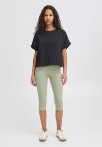 Fekete rövid ujjú cropped póló, világoszöld bordázott leggingsszel párosítva, fehér sportcipőkkel és texturált felülettel.